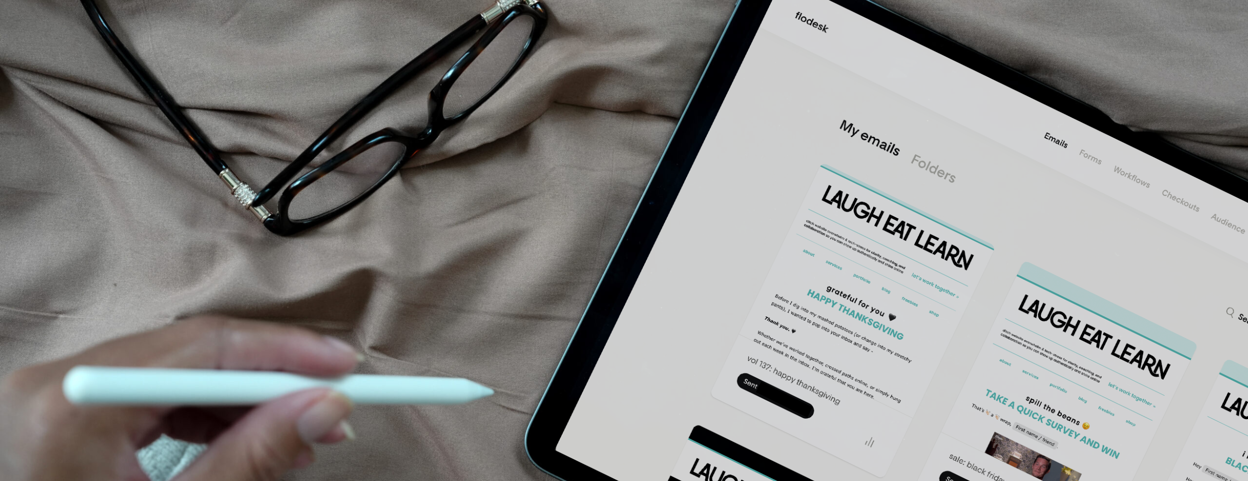 Flodesk email templates displayed on a tablet for Laugh Eat Learn, showing clean branded newsletter designs, with glasses and a stylus nearby.